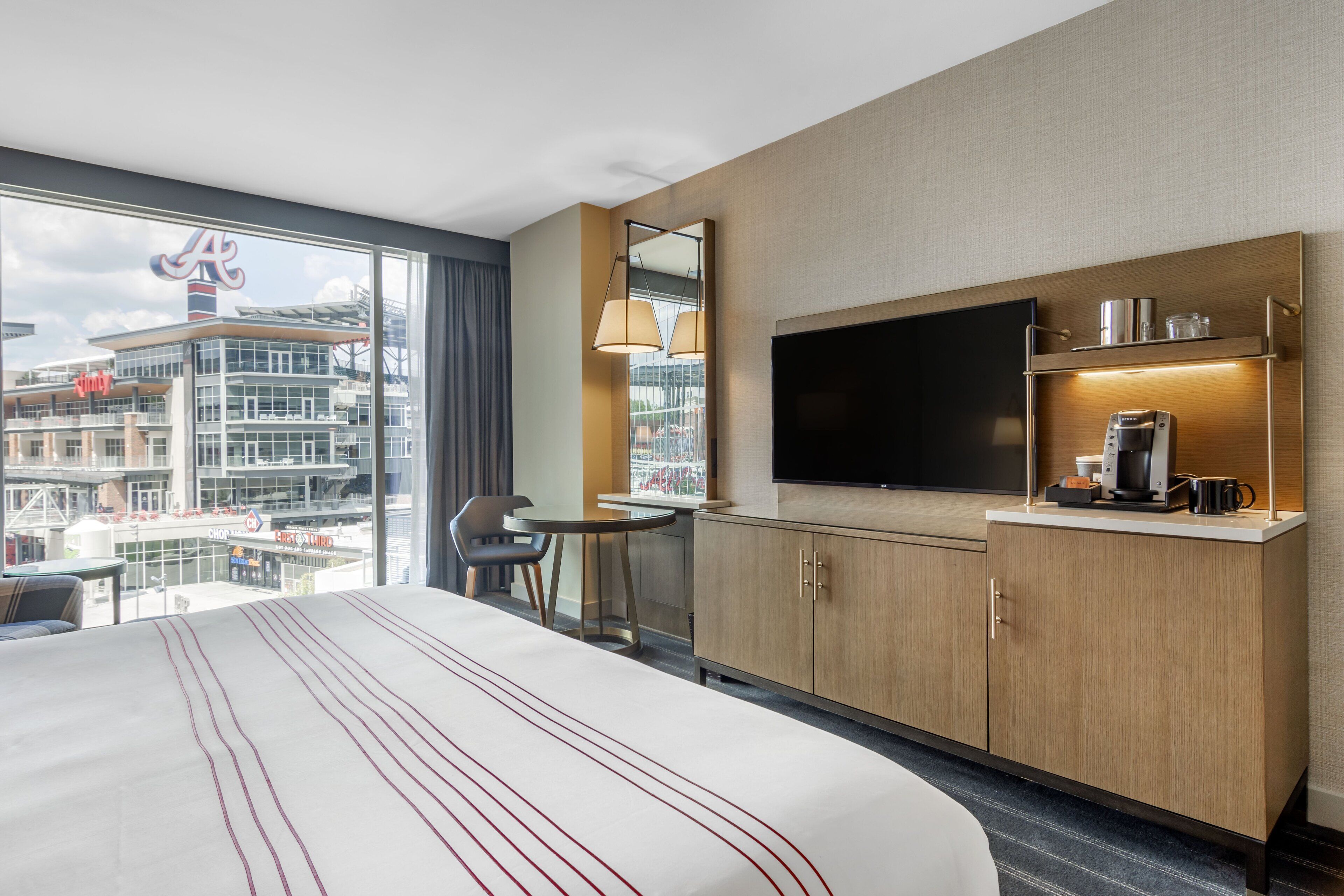 A hotel room with a large bed, a TV, a coffee machine, and a view of a cityscape.