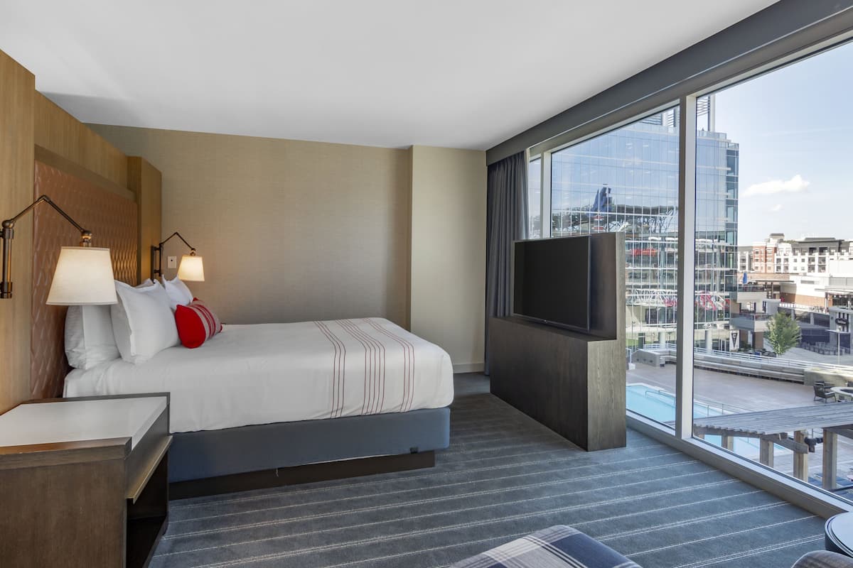 Une chambre d’hôtel équipée d’un lit, d’une télévision, d’un bureau et d’une grande fenêtre donnant sur la ville.