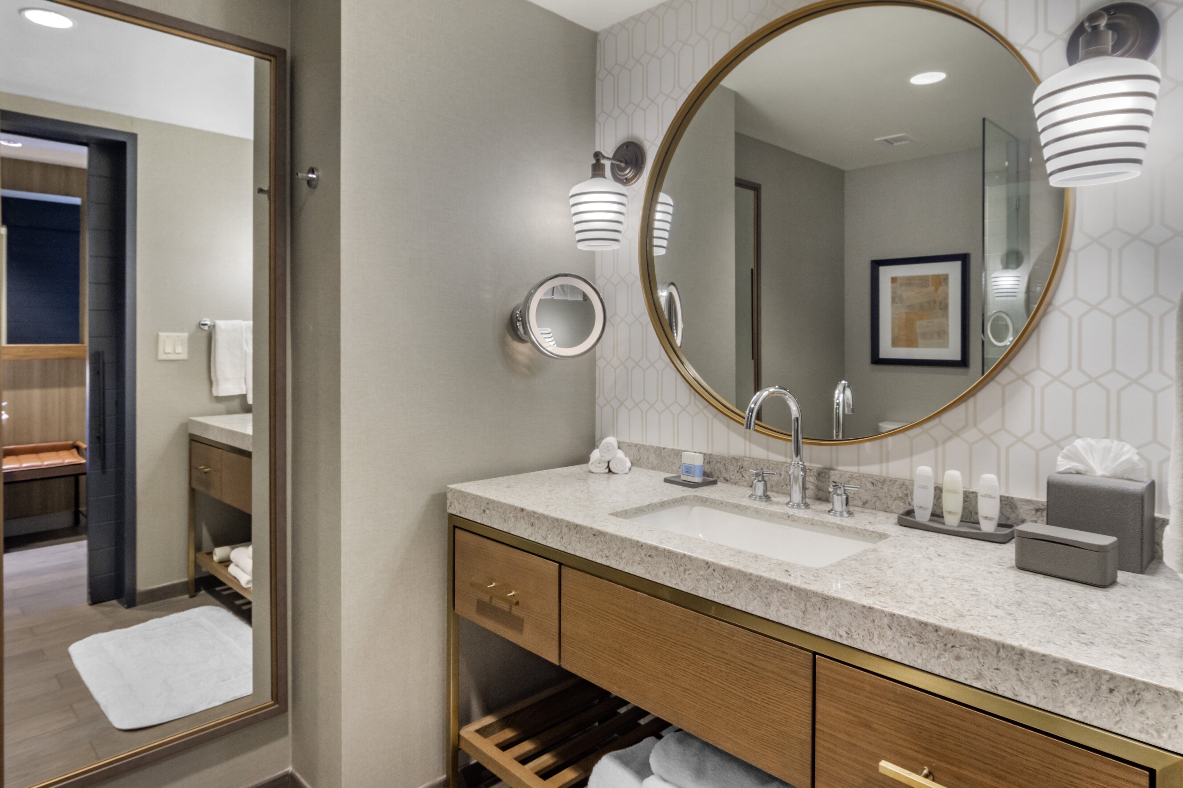 A modern bathroom with a large mirror, two sinks, and a vanity with a towel rack.