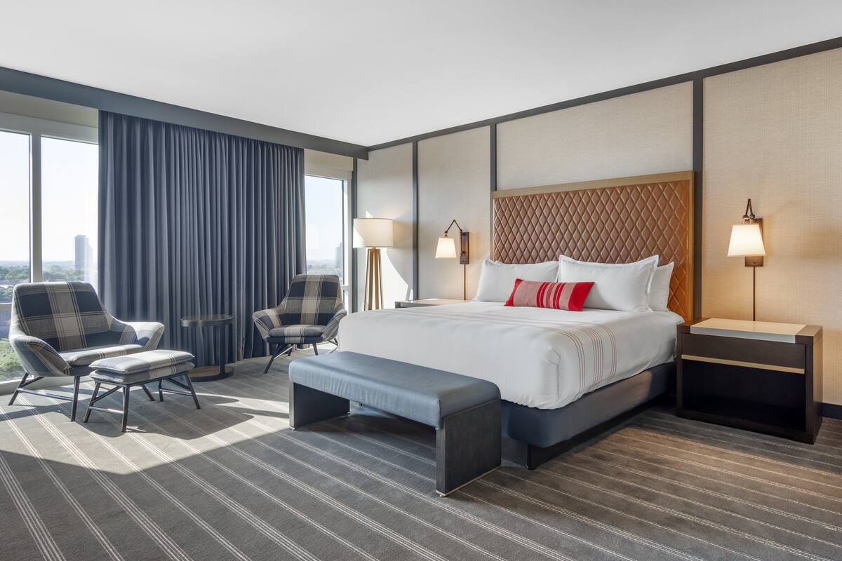 Une chambre d’hôtel moderne avec un grand lit, deux fauteuils, un banc et une table de chevet.