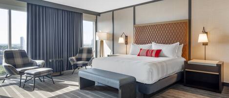Una habitación de hotel moderna con una cama grande, dos sillones, un banco y una mesita de noche.