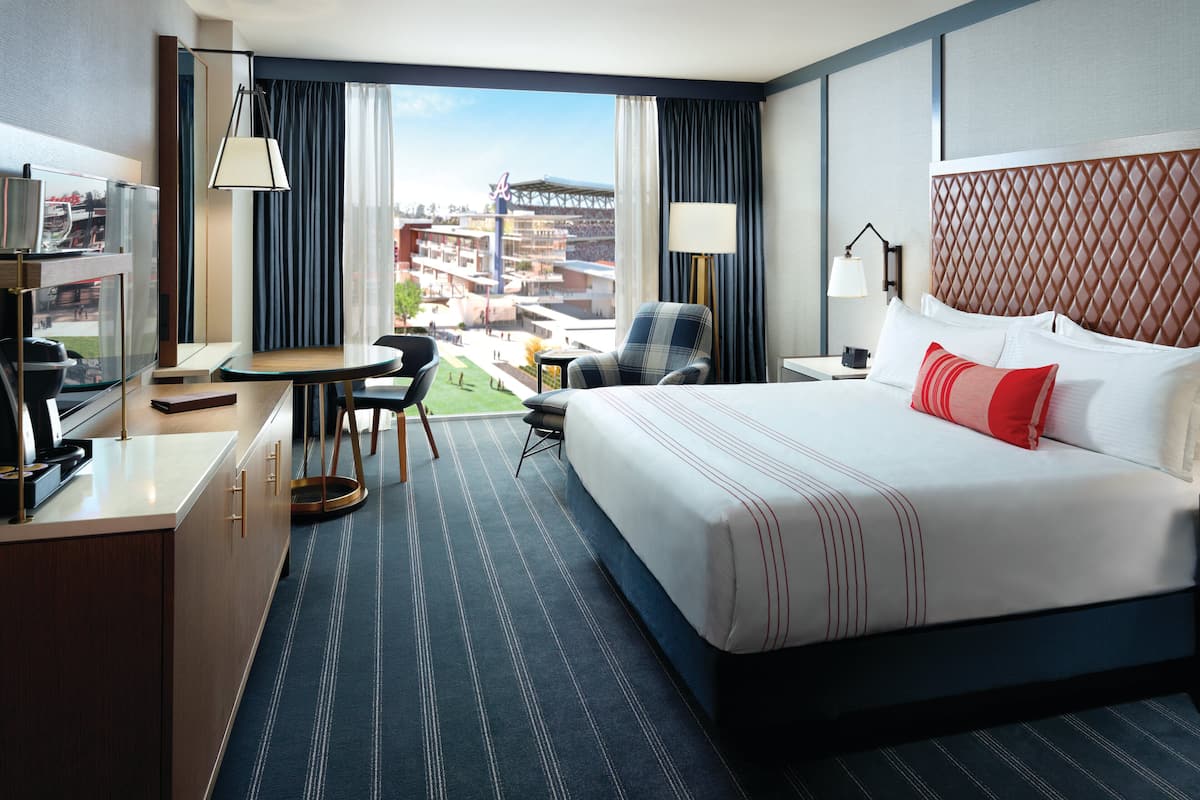 Une chambre d’hôtel avec un grand lit, un bureau avec une chaise, une télévision et une vue sur un stade.
