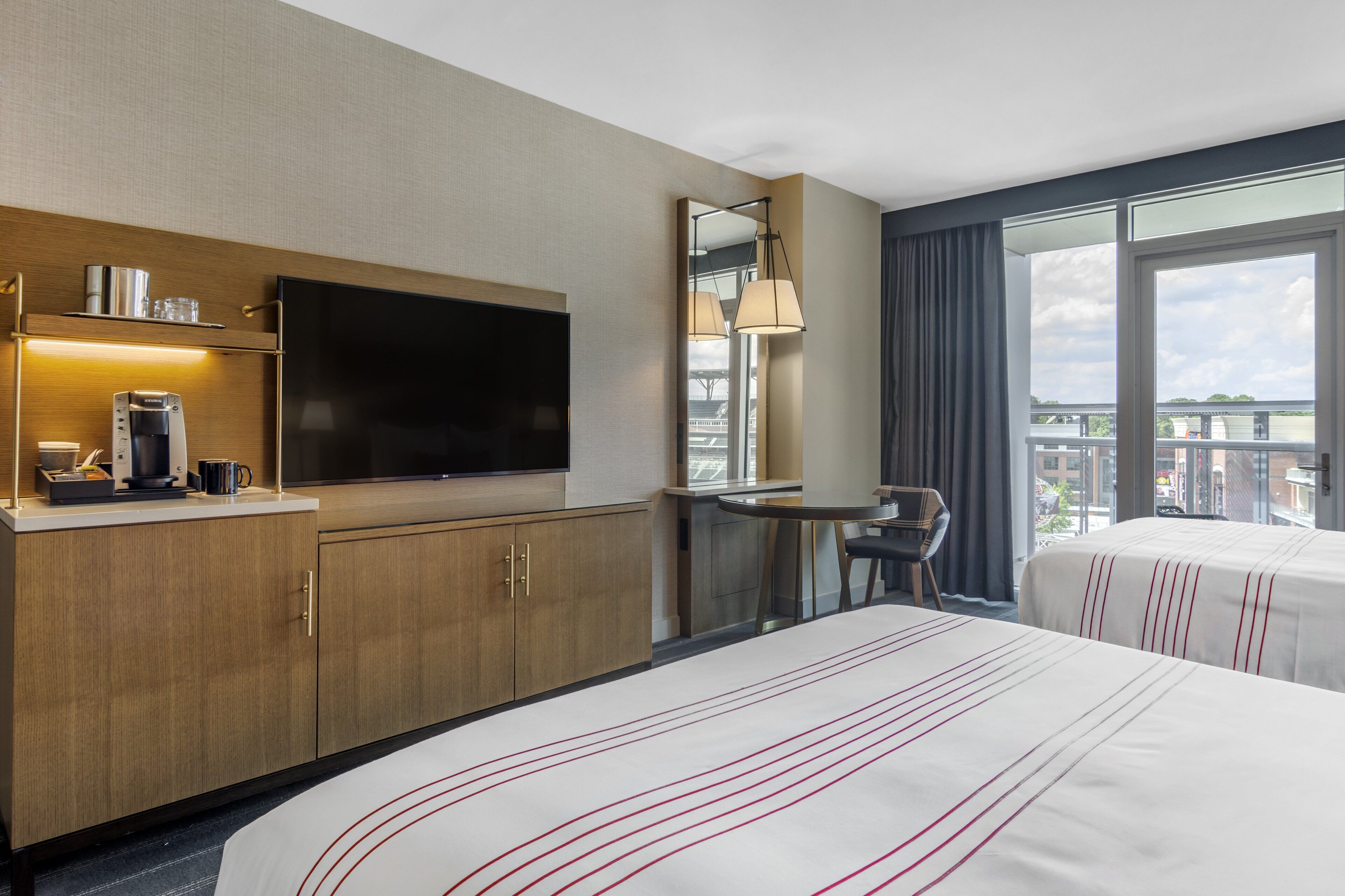 A hotel room with a large bed, a flat-screen TV, a coffee machine, a desk, and a chair.