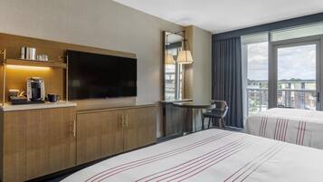 A hotel room with a large bed, a flat-screen TV, a coffee machine, a desk, and a chair.