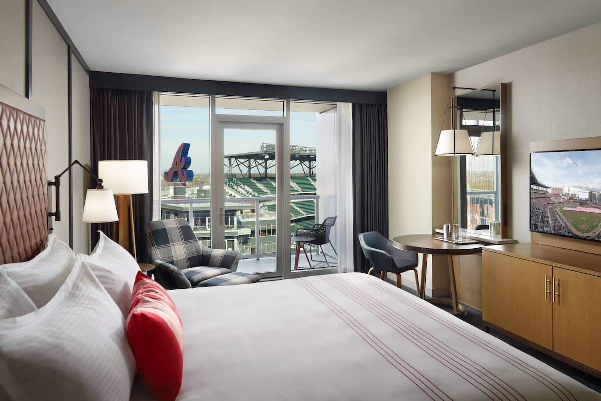 Une chambre d’hôtel avec un grand lit, un bureau, une chaise et une vue sur un stade par la fenêtre.