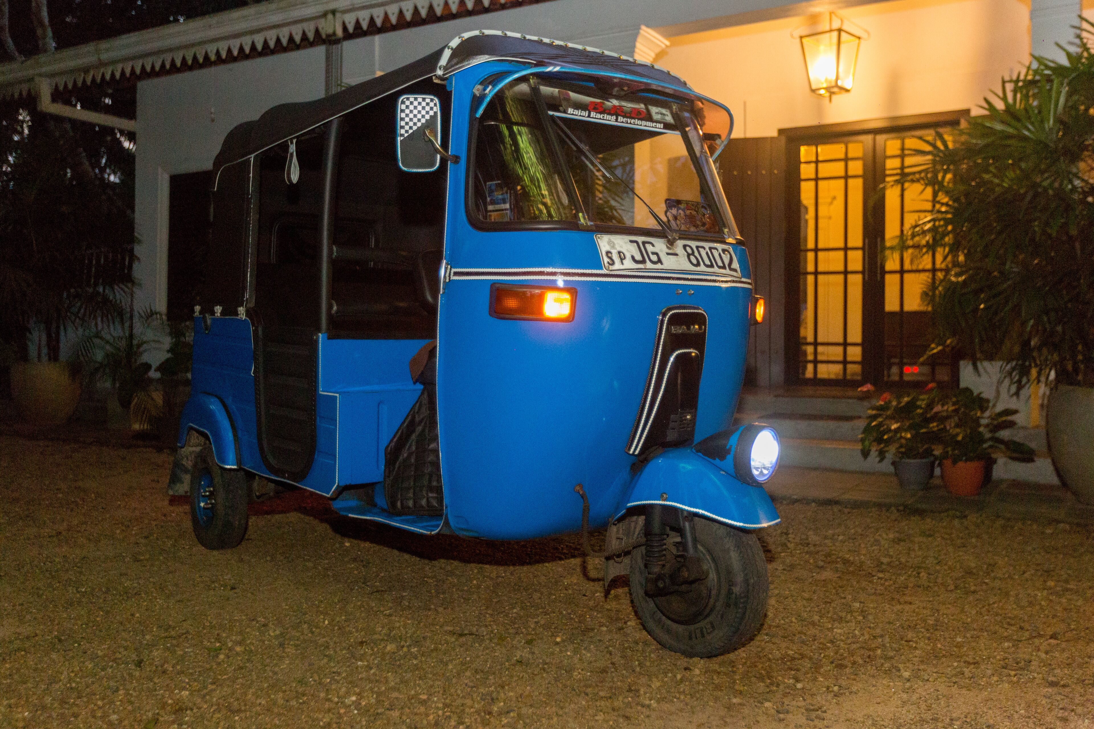 Un auto-rickshaw bleu est garé devant un immeuble dont l’entrée est illuminée.