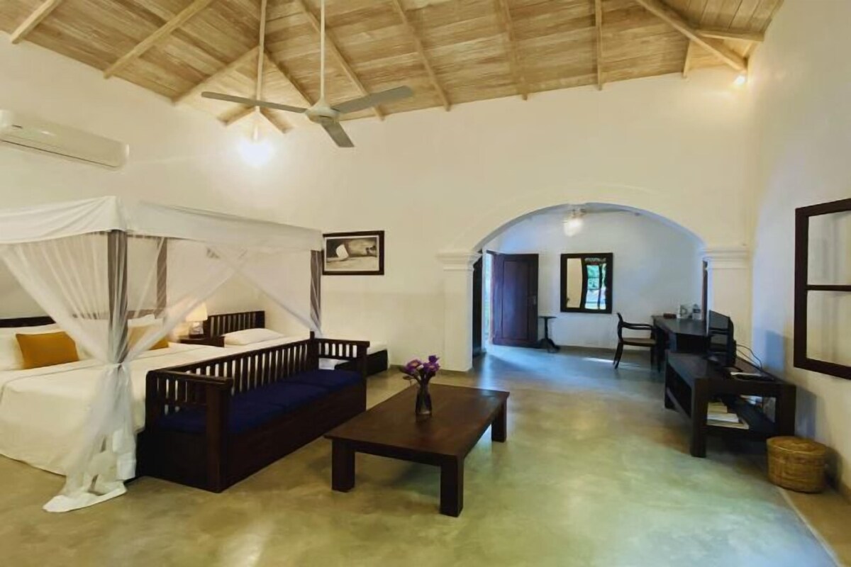 A spacious living area with a high ceiling, a bed with a canopy, a coffee table, and a seating area.