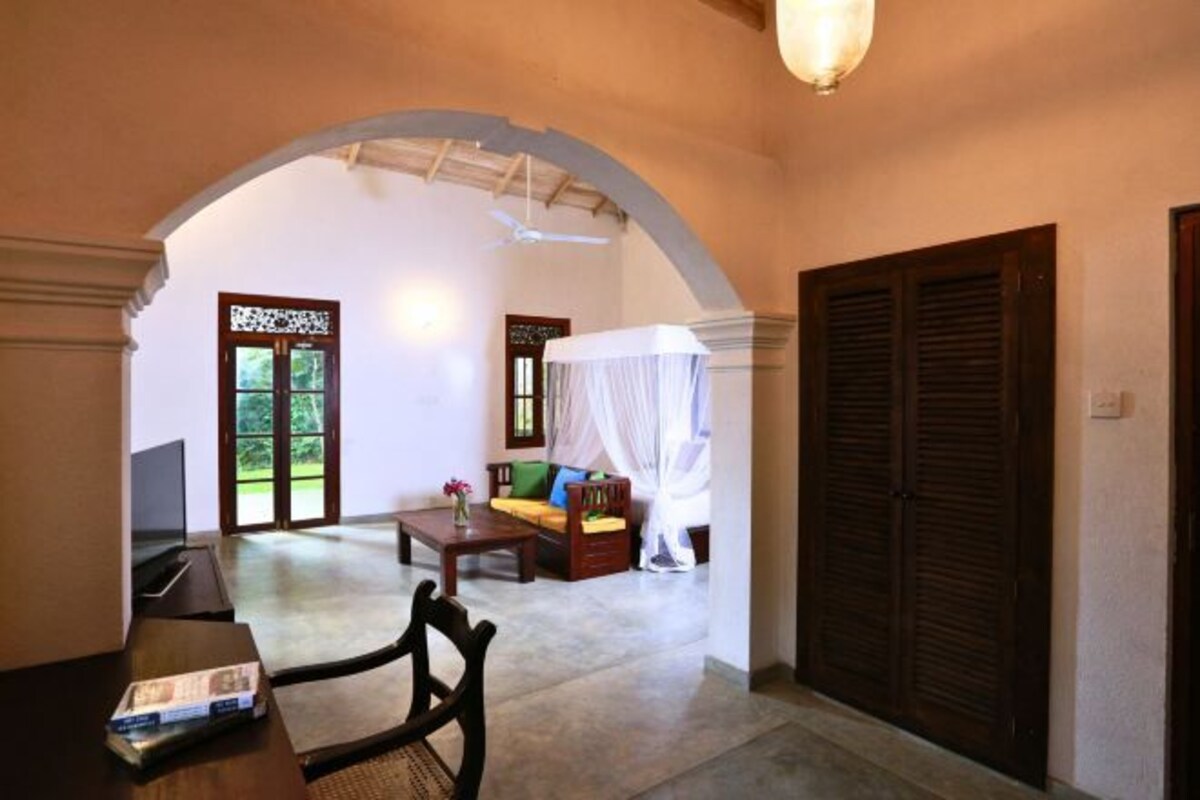 A room with a large arched doorway leading to a balcony, a sofa with a canopy, a wooden table, and a television.