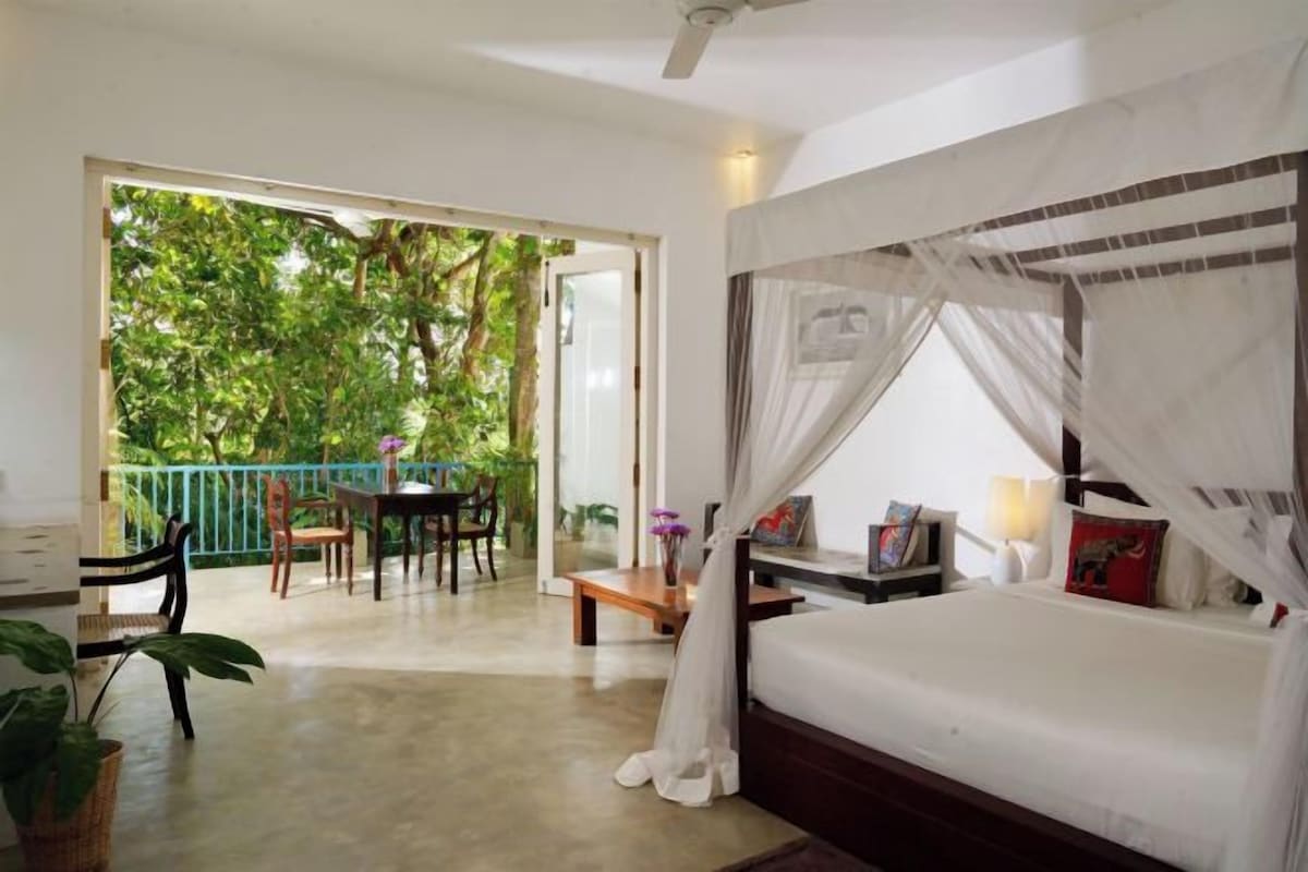 A bedroom with a bed, a balcony, and a dining area.