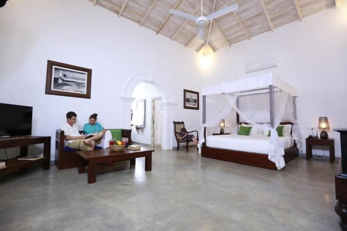 A spacious room with a large bed, a television, and a dining area.