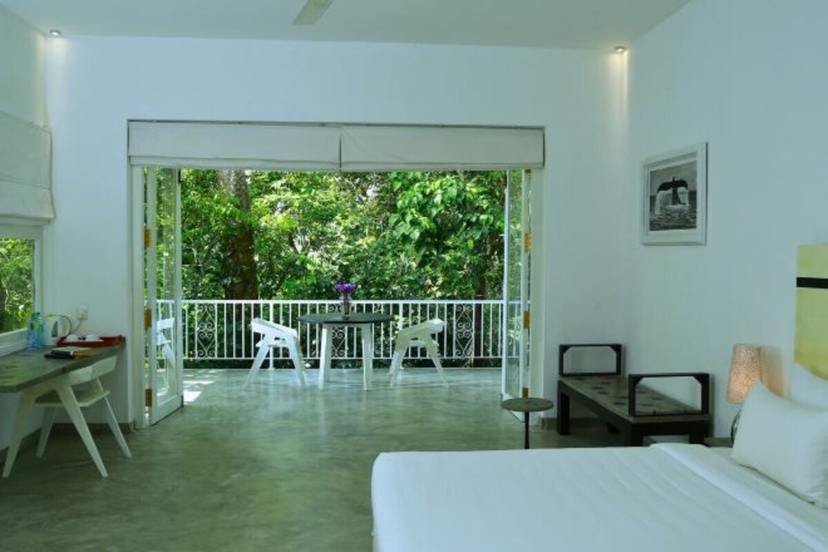 A room with a bed, a desk, and a balcony with chairs.