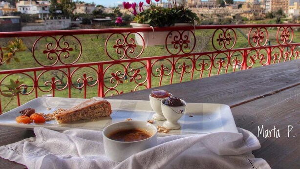 Un balcón con una mesa dispuesta para el desayuno, que incluye una rebanada de pastel, un bol de mermelada y una taza de café.