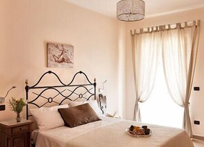 A bedroom with a bed, a bedside table, a lamp, a painting on the wall, and a window with curtains.