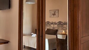 Una habitación con cama, una mesita de noche con lámpara, un televisor montado en la pared y un adorno sobre la cama.