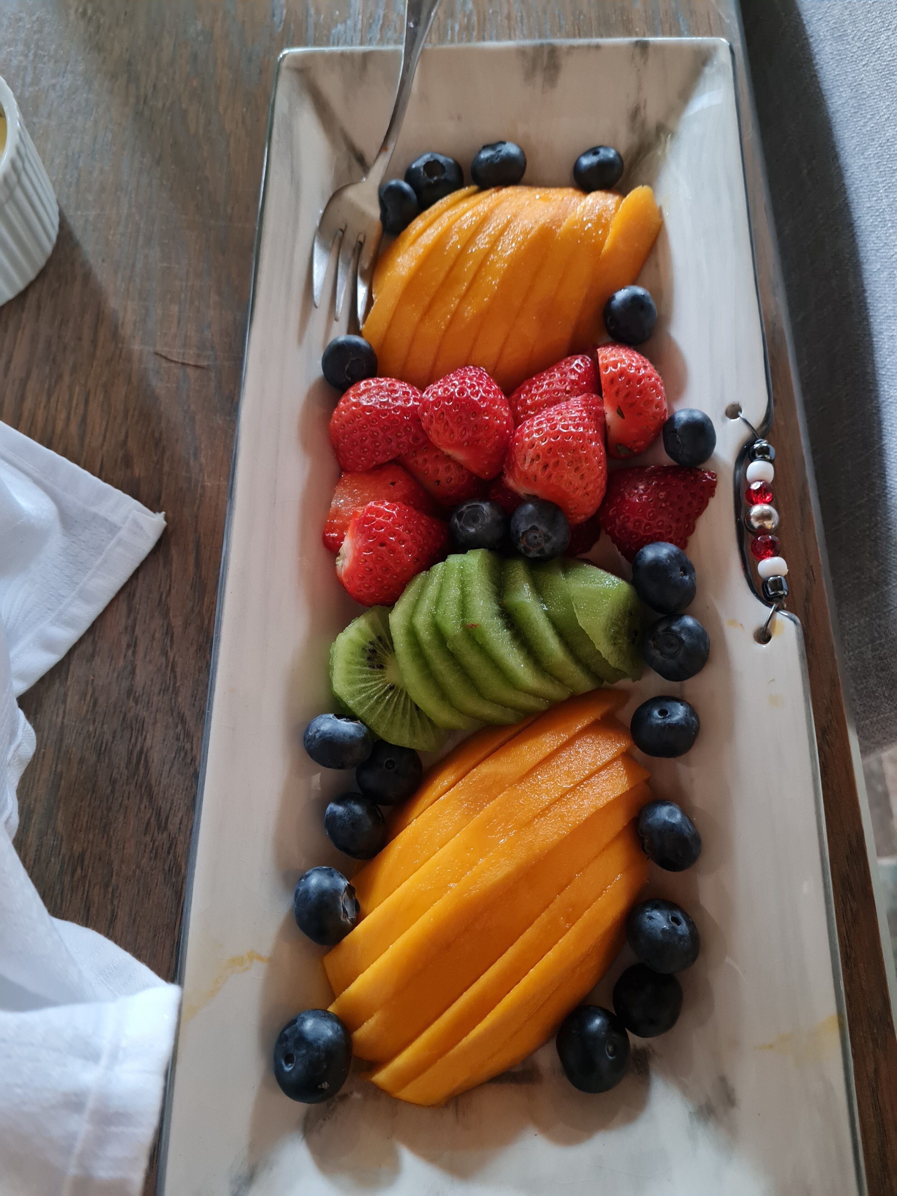 Un plato rectangular con rodajas de mango, fresas, arándanos y kiwi dispuestos en filas alternas.