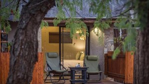 A cozy outdoor seating area with two chairs and a small table, a bed with a window, and a wooden fence. - The Dreamcatcher Lodge (Hoedspruit)
