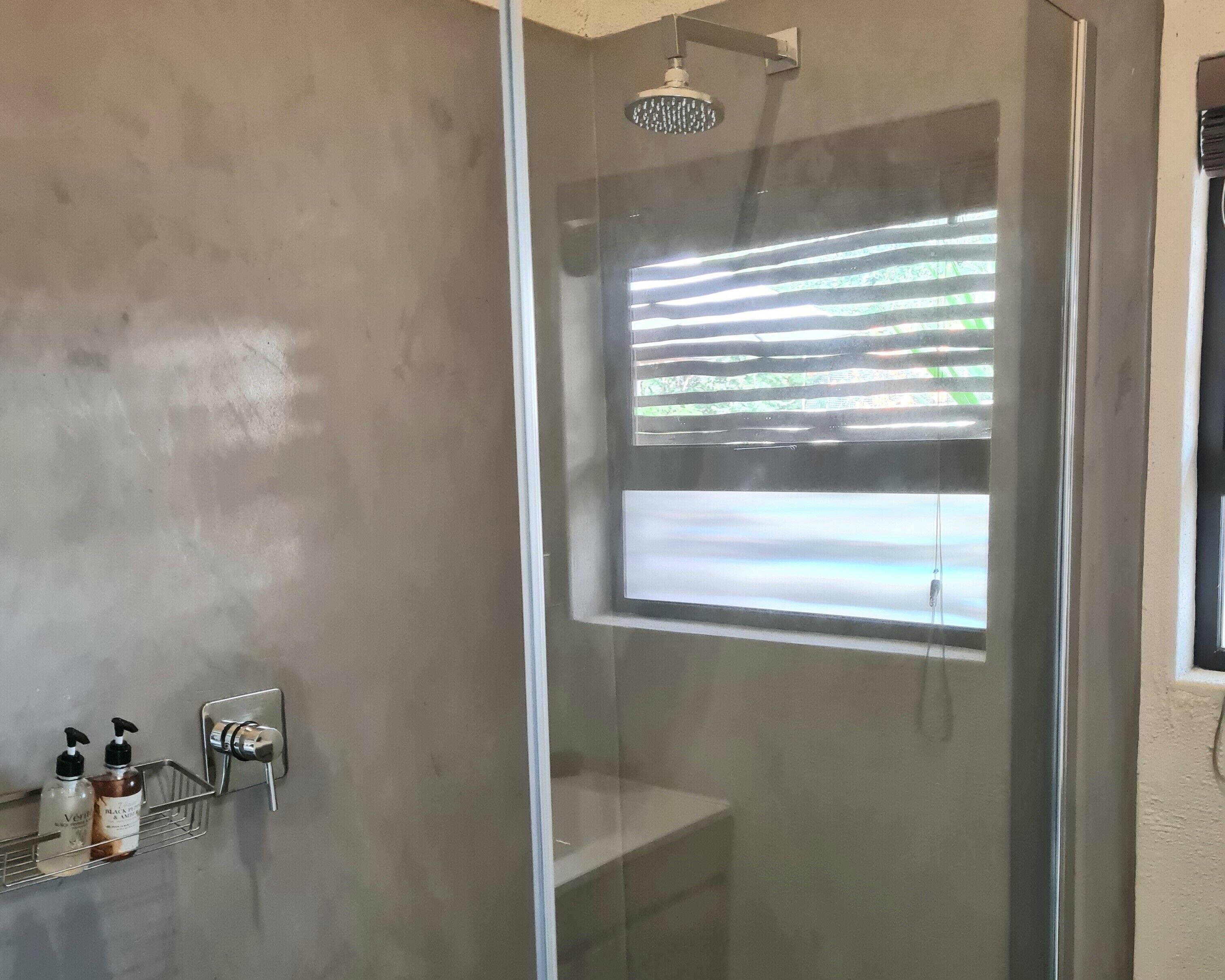 Eine Dusche mit Glastür, ein Handtuchhalter mit Flaschen und Blick auf Bäume durch das Fenster.