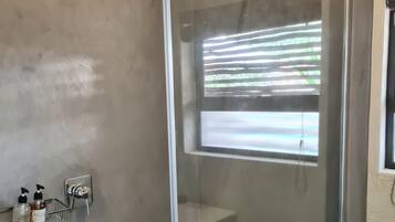 Eine Dusche mit Glastür, ein Handtuchhalter mit Flaschen und Blick auf Bäume durch das Fenster.