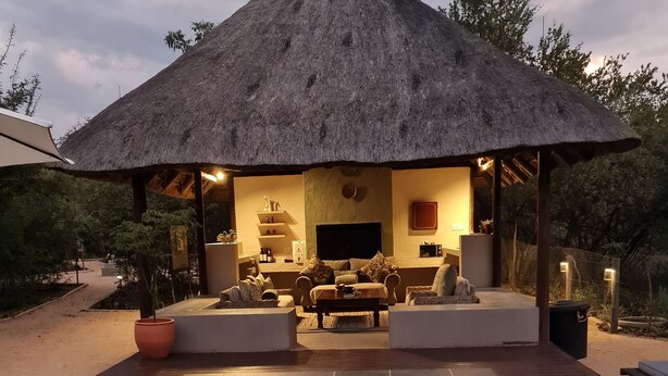 A pool area with a thatched-roof structure, seating, and a flat-screen TV. - The Dreamcatcher Lodge (Hoedspruit)