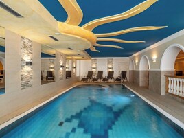 Una piscina interior con diseño moderno, que presenta una estructura de techo original y zonas de estar a lo largo de los bordes.