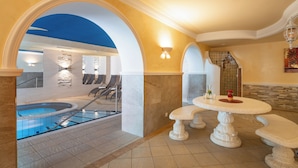 Een wellnessruimte met een jacuzzi, zitplaatsen en een tafel met een vaas en bloemen.
