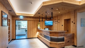 Een receptiebalie met houten afwerking, een flatscreen televisie aan de wand en een bord met kamer nummers.
