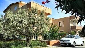 A multi-story building with a flag, surrounded by trees and a parked car.