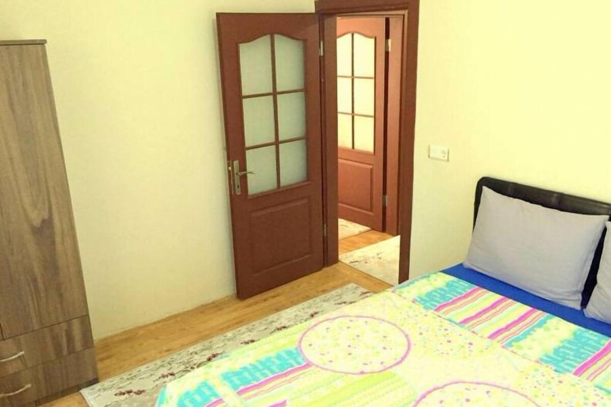 Quarto com cama, guarda-roupa e porta que dá para outro espaço.