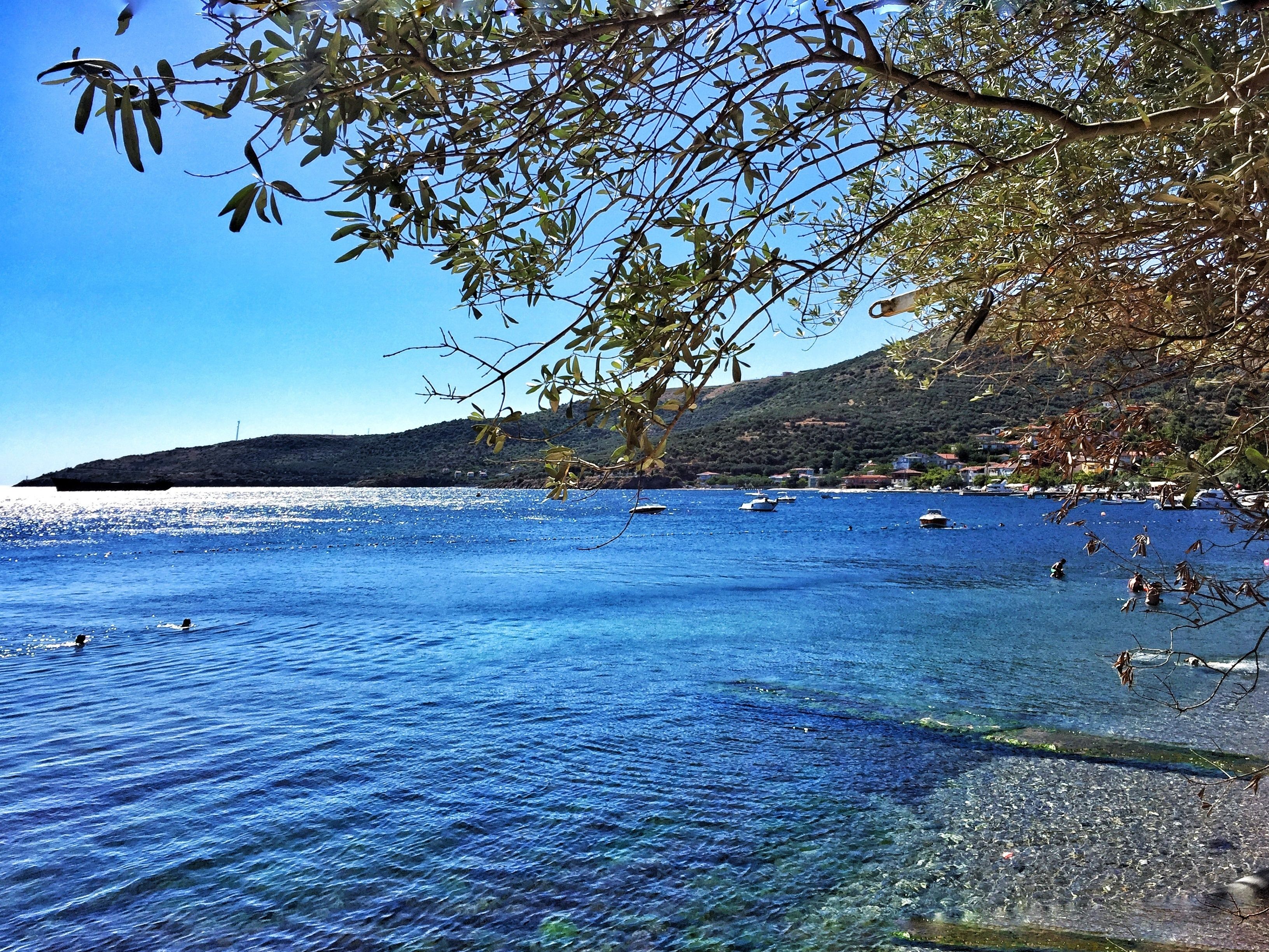 Escena costera con aguas azules cristalinas, barcos y un paisaje montañoso al fondo.