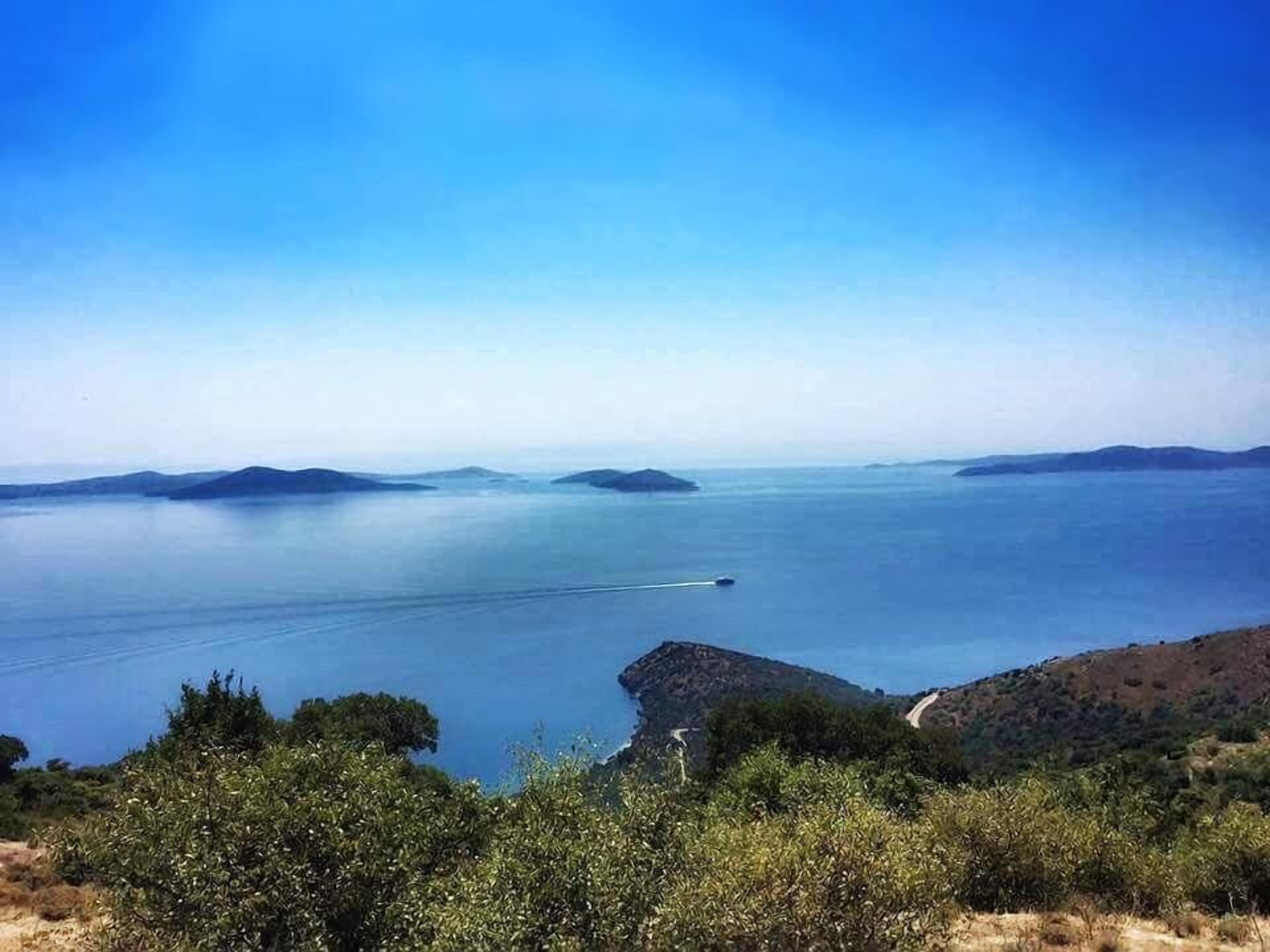 Un paysage côtier offrant une vue dégagée sur la mer, des îles lointaines et une route serpentant à travers les collines.