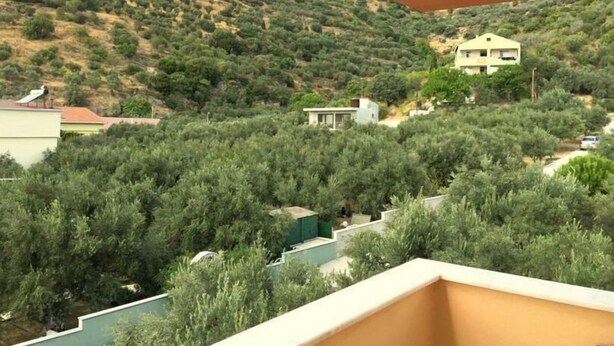 A balcony with a view of a hillside with sparse vegetation and a few buildings.