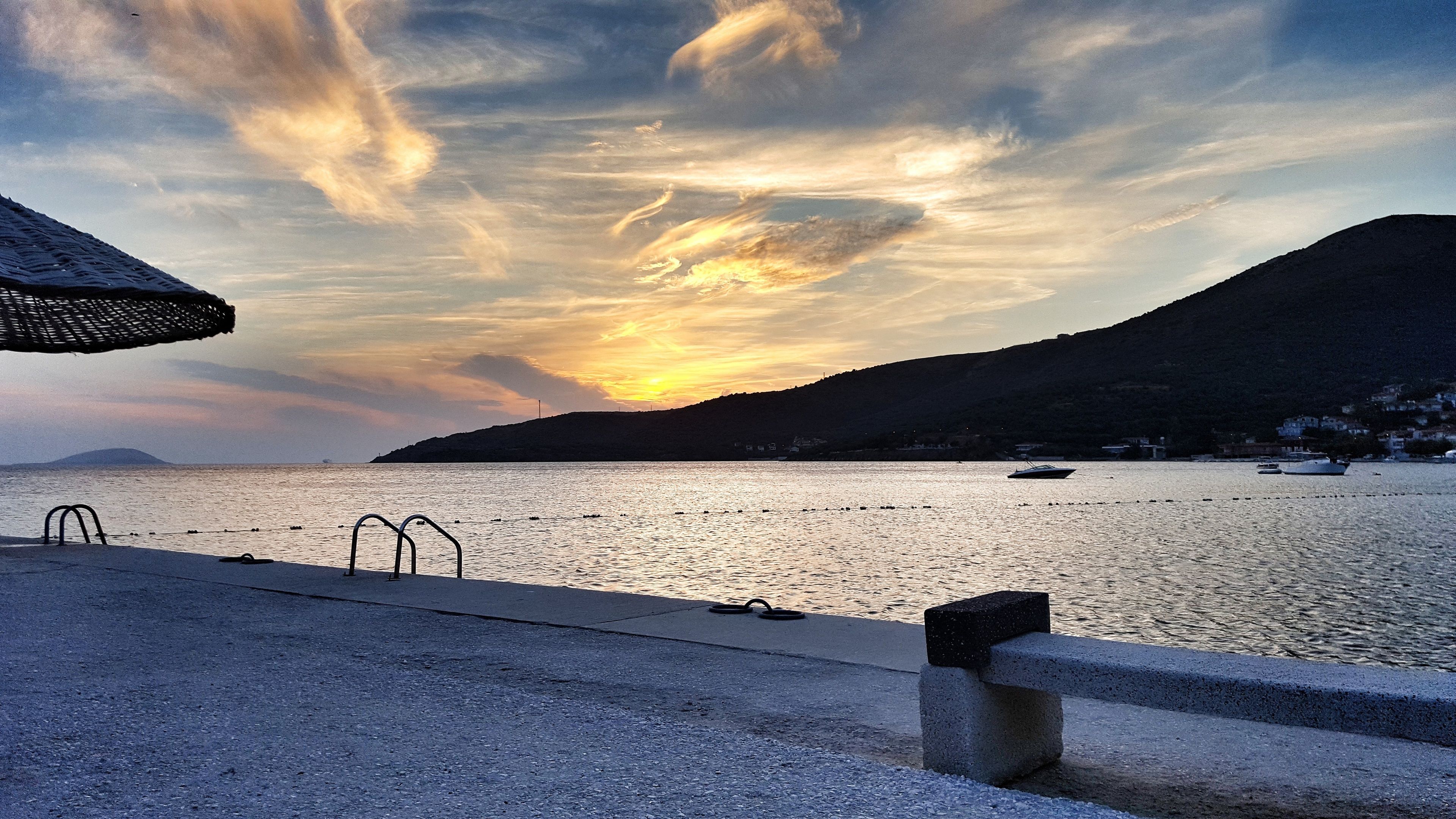 Vista costera con atardecer, mar en calma y montañas al fondo.