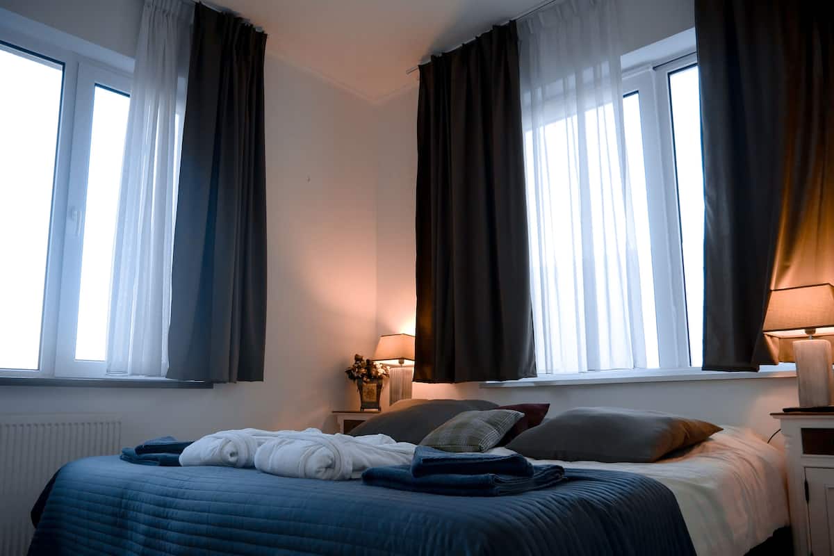 A bedroom with a bed, two bedside tables, a lamp, and a window with curtains.