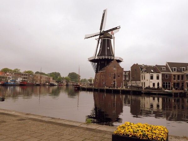 A traditional windmill by a calm river, surrounded by historic buildings and boats.