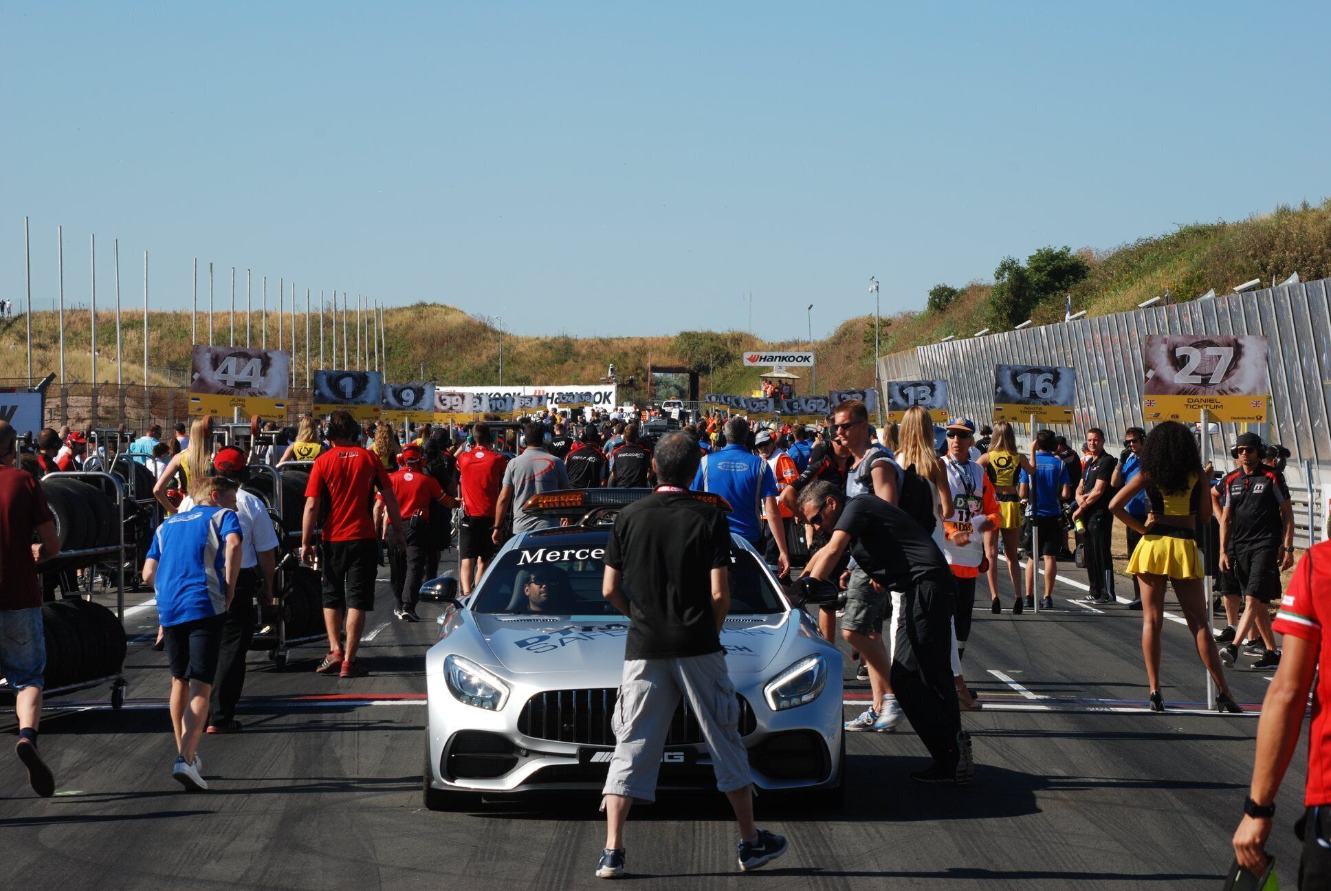 A crowd of people gathered around a silver sports car with the word "Merc" on the hood.