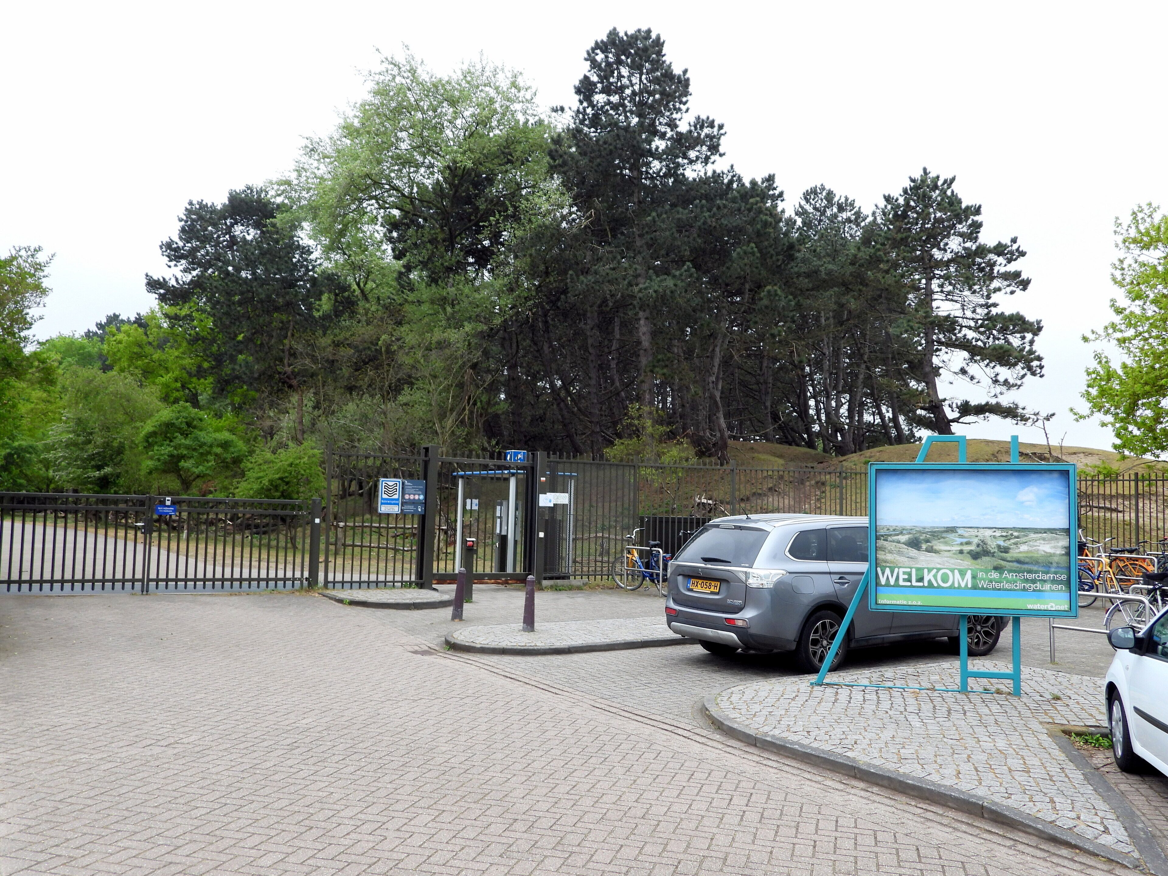 A paved entrance with a metal gate, a car, and a welcome sign.