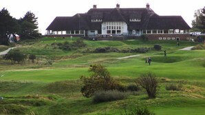 A large building with a thatched roof, likely a clubhouse or hotel, situated on a golf course with a well-maintained lawn and a few trees. - Pension Villa Tanahlot (Zandvoort)