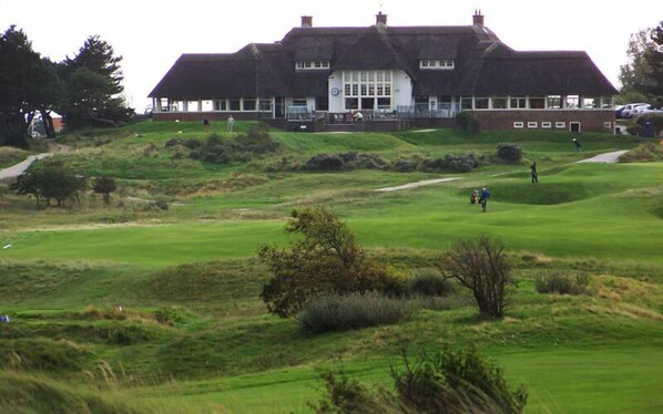 A large building with a thatched roof, likely a clubhouse or hotel, situated on a golf course with a well-maintained lawn and a few trees. - Pension Villa Tanahlot (Zandvoort)