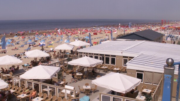 A beachside cafe with outdoor seating and umbrellas, overlooking a crowded beach. - Pension Villa Tanahlot (Zandvoort)