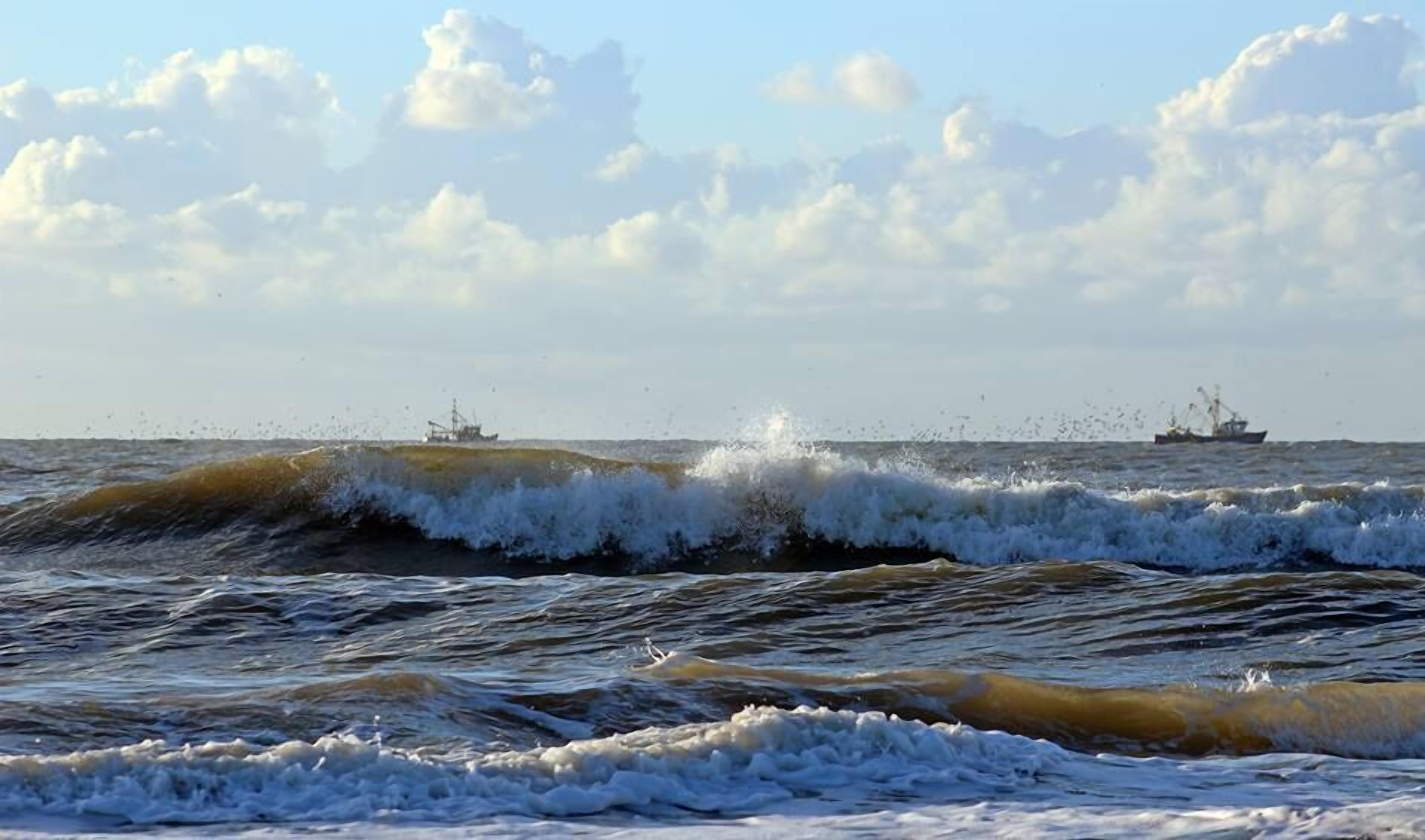 Blick auf das Meer mit Wellen und zwei Schiffen in der Ferne.