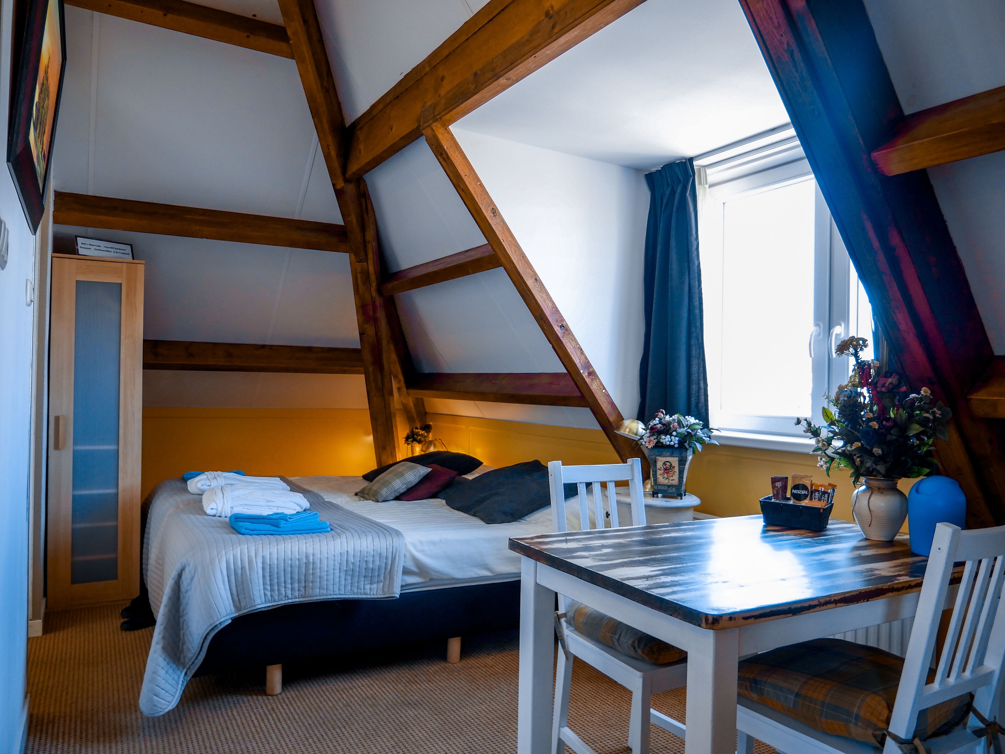 A cozy attic bedroom with a bed, a small table, and a window with curtains.
