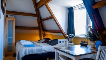 A cozy attic bedroom with a bed, a small table, and a window with curtains.