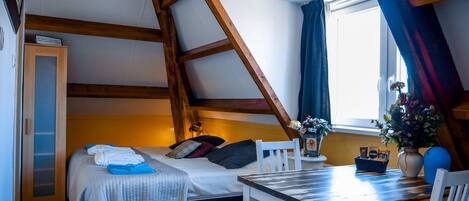 A cozy attic bedroom with a bed, a small table, and a window with curtains.