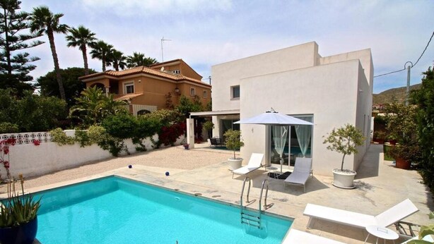 A modern pool area with a clear blue pool, lounge chairs, and a small building with a glass door. - Villa Nathalie (El Campello)