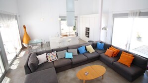 A modern living room with a sectional sofa, a coffee table, and a dining area with a bar. - Villa Nathalie (El Campello)