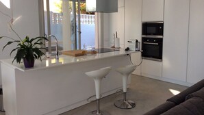 A modern kitchen with white cabinetry, a built-in oven, and a bar area with two white bar stools. - Villa Nathalie (El Campello)