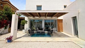 A modern outdoor patio with a covered seating area, a pergola, and a view of the adjacent building. - Villa Nathalie (El Campello)