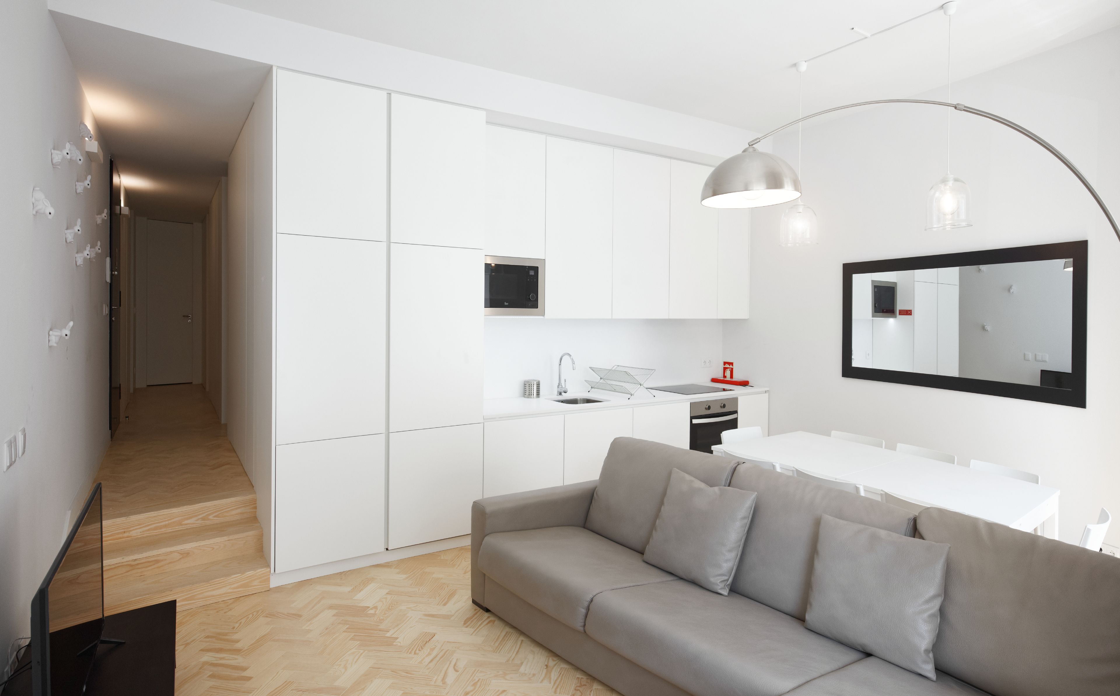 A modern kitchen with white cabinets, a built-in oven, and a dining area with a white table and sofa.