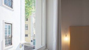 A hotel room with a large window, a bed, and a bedside table. - City Stays Sé Apartments (Lisbon)