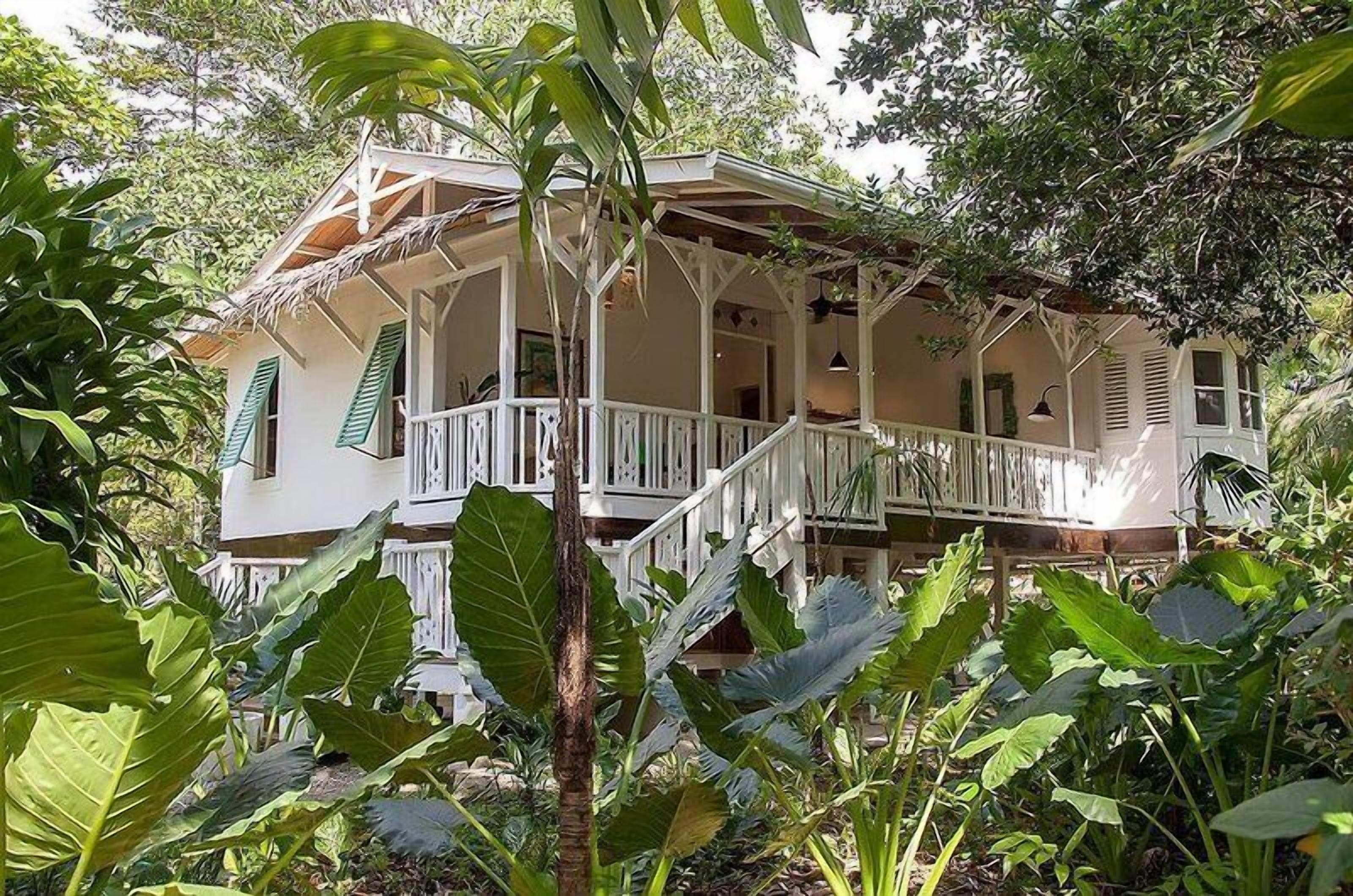 A two-story house with a balcony, surrounded by lush greenery.